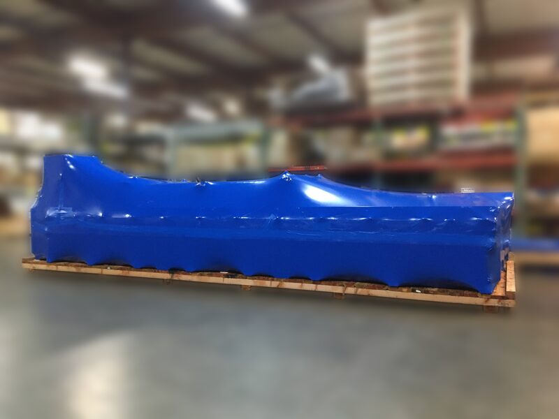 A long wrapped load on a timber skid inside the warehouse with pallets stacked behind.