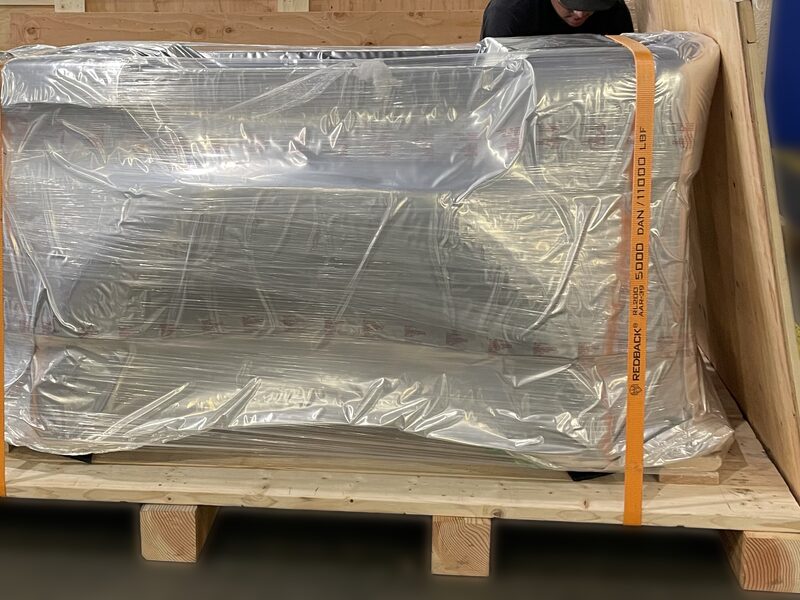 A wrapped load strapped down on a heavy timber skid with the runners visible underneath.