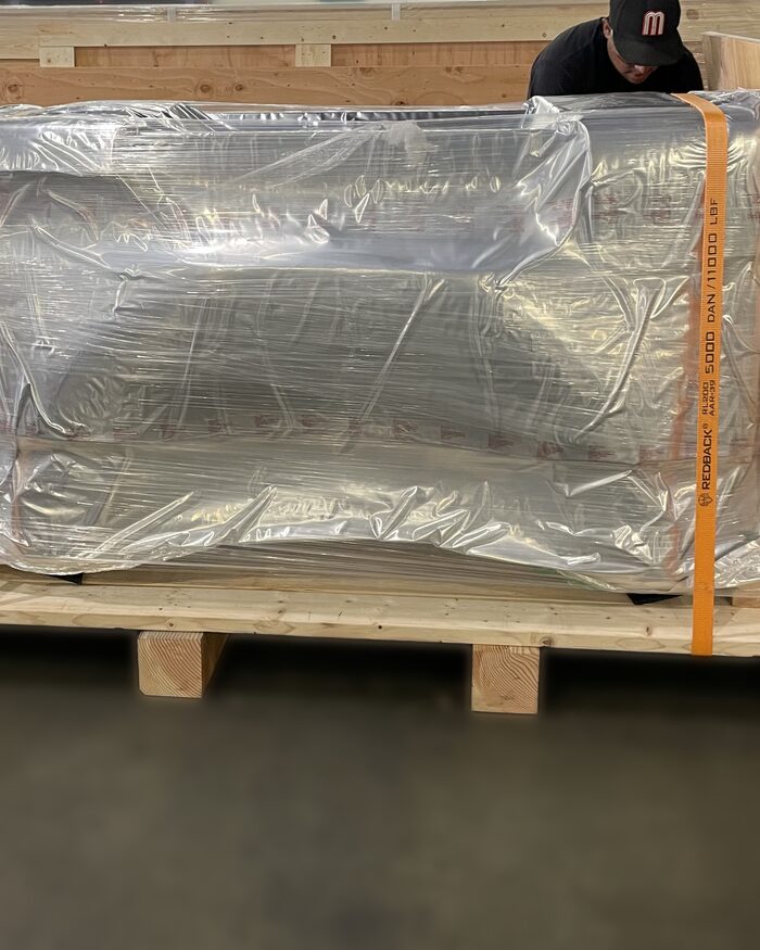 A wrapped load strapped down on a heavy timber skid built in the shop, with the runners visible underneath.